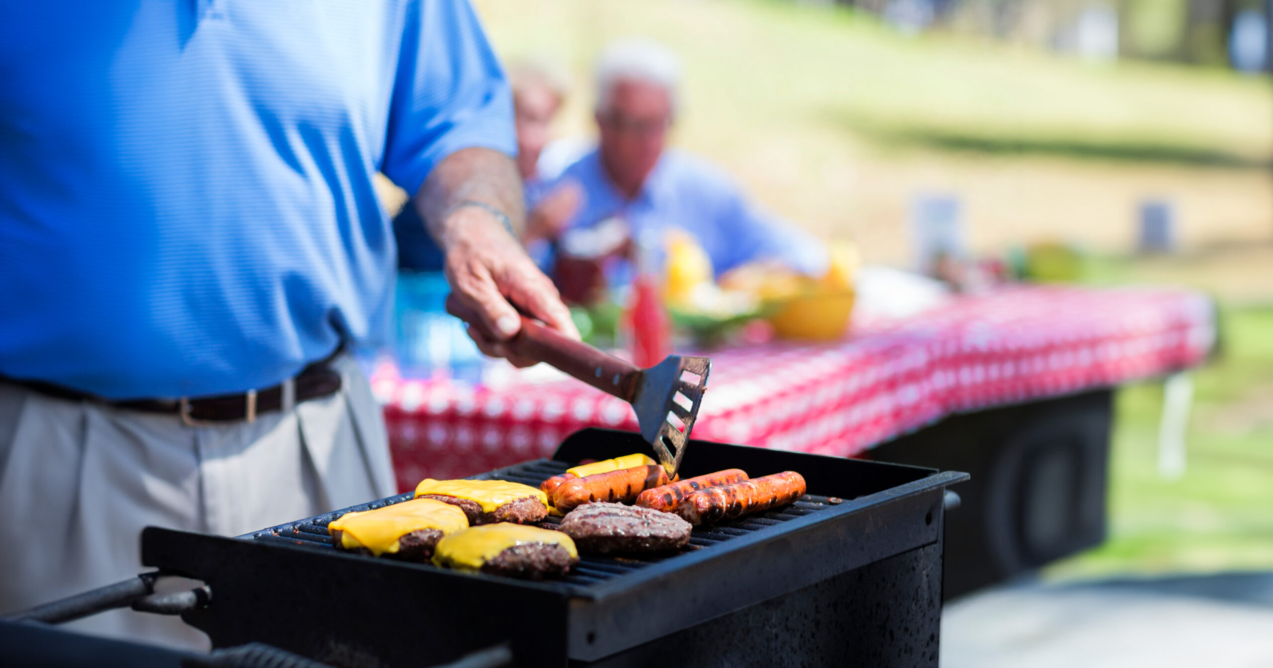man grilling hamburgers and hot dogs at a picnic